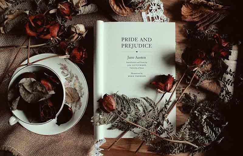 Pride and Prejudice book open on table with roses and cup of tea.